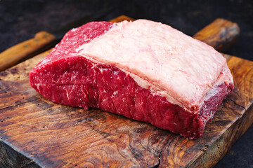 Raw dry aged wagyu roast beef steak offered as close-up on a old rustic wooden board