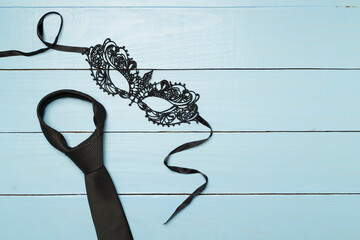 Lace mask and tie on wooden background, top view