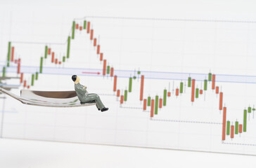 A miniature figurine of a businessman sits on a spoon and looks at quotes charts.