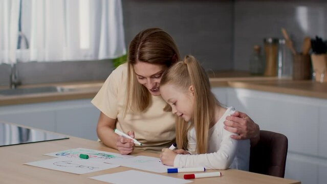 Kids development at home. Happy loving mother drawing pictures with her little daughter, having fun together at kitchen
