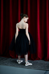 A cute ballerina girl in a black dress on a red background. Art. Dance. Beauty.