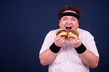 Sport, fitness and healthy lifestyle. Funny fat guy goes in for sports and eats a hamburger.	