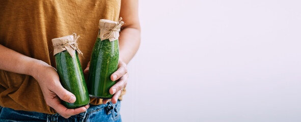 Female hands hold bottles of freshly made green smoothie, copy space. Delivery of fresh drinks