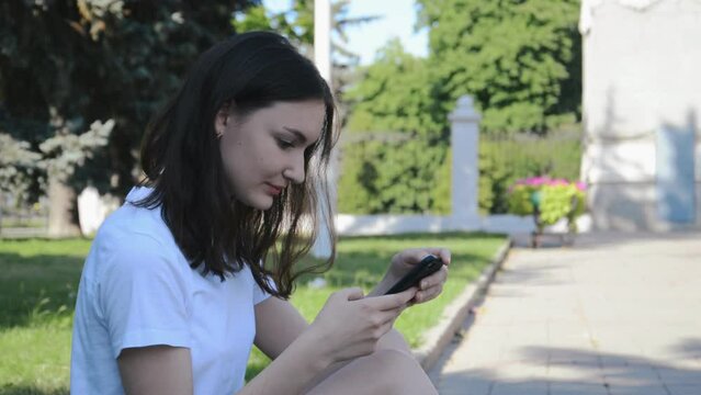 A beautiful girl in the park writes a message on her phone
