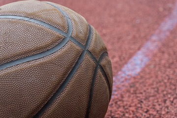 Close-up basketball ball on the red court. Basketball on the street or indoor court. Sports gear without people. Template, sport background