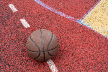 Close-up basketball ball on the red court. Basketball on the street or indoor court. Sports gear without people. Template, sport background