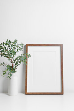 Wooden portrait frame mockup with fresh eucalyptus twig decoration