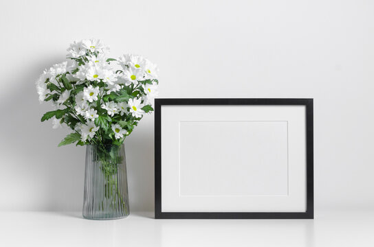 Black frame mockup in white minimalistic interior with fresh flowers bouquet