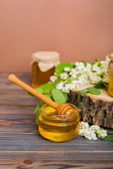 Sweet honey jar surrounded spring acacia blossoms. Honey flows from a spoon in a jar. jars of clear fresh acacia honey on wooden background