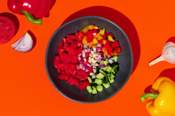 Ingredients in a bowl for tomato gazpacho soup on orange background.