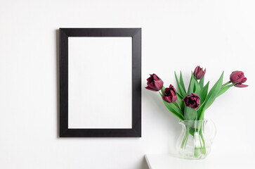 Black portrait frame mockup on white wall interior with red spring tulips flowers