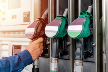 A man at a gas station taking the fuel nozzle off the fuel dispenser unit to fill the tank of his...