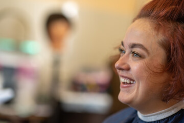 A brown-haired girl is sitting in a chair at the hairdresser doing her hair and styling her hair.