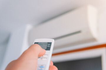 Fototapeta premium A person's hand pushing the remote control of an air conditioner in the middle of a heat wave. Person using an indoor hot air pump in a house. Technology concept.