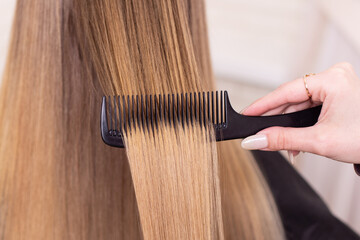 Fototapeta premium Hairdresser's hand brushing long natural blonde hair in beauty salon