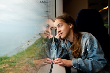 A young girl looks out the window of a train at the sea. Journey. Reflection. Vacation. Summer. Family vacation.