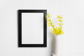 Black portrait frame mockup on white wall interior with yellow spring flowers in vase