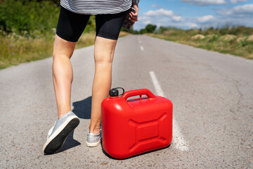 A car parked on the side of the road, an empty red canister. The girl stops on the road to fill up the car. Fuel shortage - oil, diesel, gasoline.