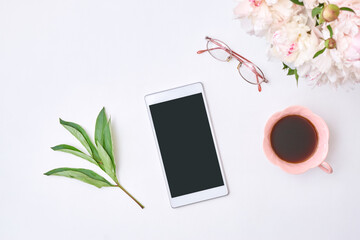 Feminine blogger workplace, smartphone with blank screen mockup, cup of coffee and white peonies on a white table. Flat lay banner, template for blog