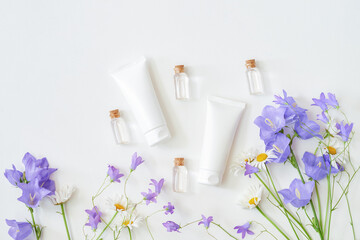 Cosmetic cream tubes packaging and wildflowers on white background. Natural skin care concept, mockup for design