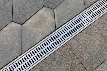 The grid of the rainwater drainage system on the sidewalk made of stone paving slabs