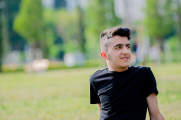 Handsome young boy in black shirt. Happy young male smiling on the grass in the park.