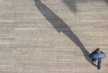 Man walking shot from above. Top aerial view man walk on across pedestrian concrete with black silhouette shadow on ground.