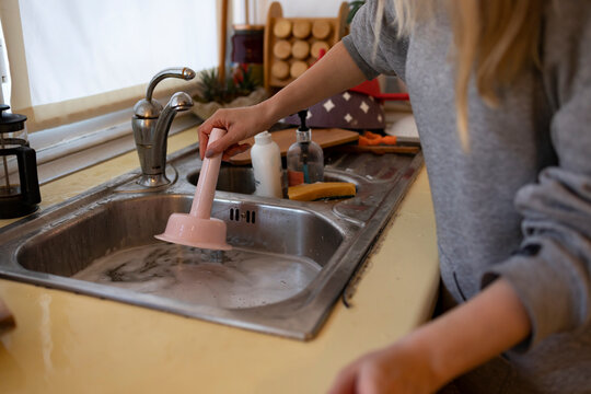 She is trying to unclog a sink with plunger. No face in photo.