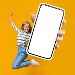 Happy woman jumping in air on orange background, showing smartphone
