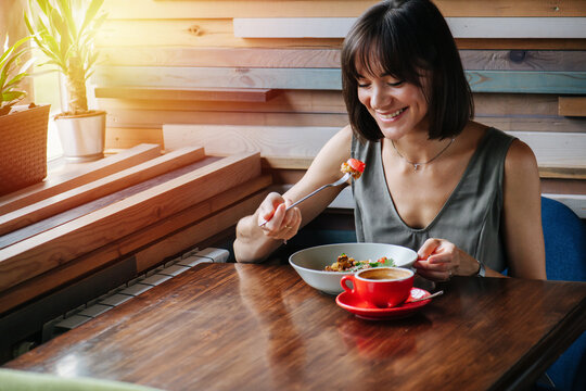 Extatic overly happy woman looking at a pieceof a pie on her fork. Sitting behind a table in a cafe. Sunlight shining from a window.