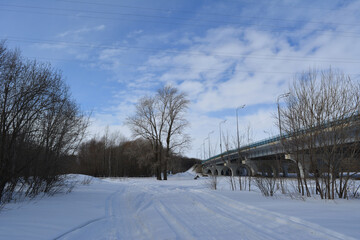 Winter landscape with bare trees and snowy road along the bridge.