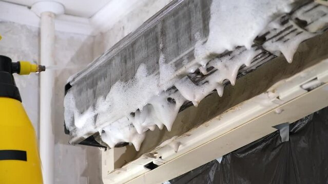 A man washes off a special foam for cleaning air conditioners with a jet of water under pressure. Split system maintenance.