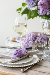 Beautiful table decor for a wedding dinner with a spring blooming lilac flowers. Celebration of a special event. Fancy white plates, wineglasses. Countryside style