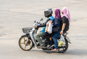 A taxi driver on a motorcycle rides with a two woman in hijab.