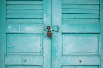 Exterior view of old vintage pale green wooden closed door which locked by padlock. 