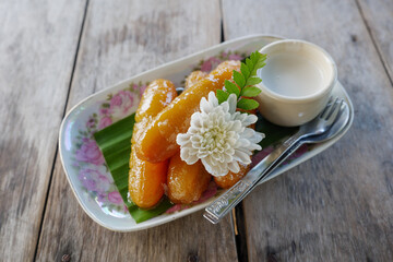 Thai style dessert, Sweet bananas serve with coconut syrup on the plate and wooden table.