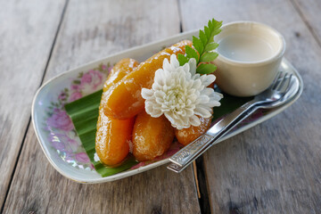 Thai style dessert, Sweet bananas serve with coconut syrup on the plate and wooden table.