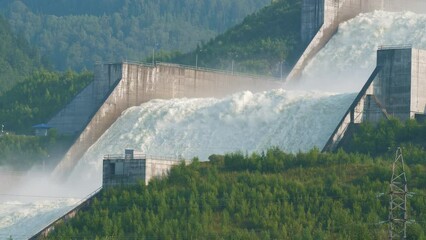 Coastal spillway of Sayano-Shushenskaya Dam on Yenisei River surrounded by forests. Passage for surplus water from hydroelectric plant. Landscape with artificial waterfall, wooded hills. Green energy