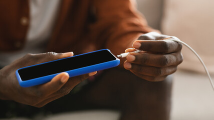 Unrecognizable african american male hands plugging a charger in modern smartphone, closeup, cropped