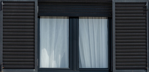 Frame of a wooden black window with white curtain and open shutters