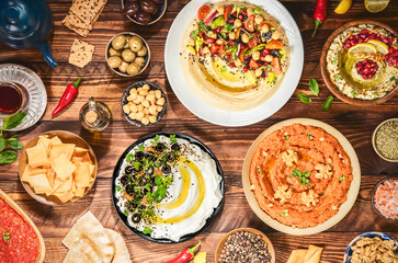 Fototapeta na wymiar Arabic Cuisine: Varieties of delicious Middle Eastern meze and dips. hummus plate, muhammara, labneh, baba ghanough, harissa and olives. Served with pita bread and fresh olive oil.