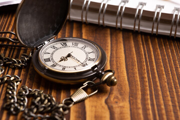 pocket watch with notepad on wooden background closeup concept