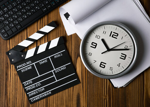 black movie clapper with keyboard and script sheets with clock on a wooden table