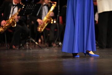 A woman in a blue long dress stands on stage performing with a brass jazz orchestra festive clothes...