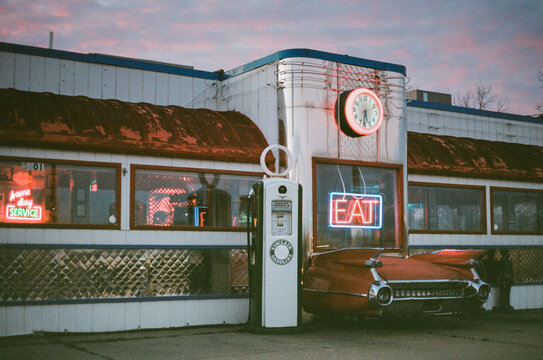 Old Diner With Neon Signs And Cadillac Car Sticking Out Of The Front