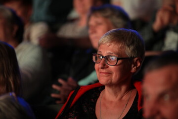 The face of a happy woman smiling elderly lady with glasses sitting in the theater auditorium at the performance.Image concept cultural leisure and recreation of people