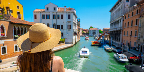 A woman with a hat standing on a bridge in Venice on a sunny summer and holiday day.