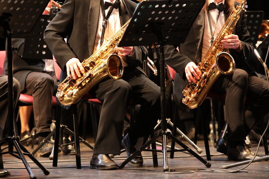 A group of saxophonist musicians playing a musical instrument saxophone concert in the orchestra sitting at the console with notes dressed in a black uniform suit background musical image close-up