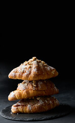 Baked croissant on a  board and sprinkled with powdered sugar, black table. Appetizing pastries for breakfast.