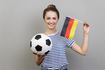 Portrait of joyful cheerful woman wearing striped T-shirt holding soccer ball and german flag,...